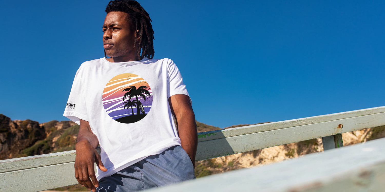 Young man wearing a Coastline summertime collection t-shirt leaning against the wooden railing of a beach walkway
